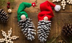 two pine cones are sitting next to christmas decorations on a wooden surface, one has a gnome's hat and the other is wearing a green elf's head