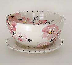 a white bowl and saucer with pink flowers painted on the side, sitting next to each other