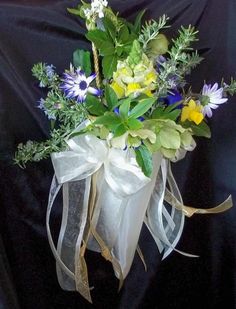 a bouquet of flowers in a vase on a black tableclothed cloth with gold ribbon