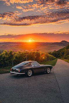 a black car parked on the side of a road at sunset with mountains in the background