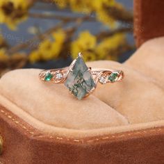 a green and white stone ring sitting on top of a brown velvet box with flowers in the background