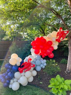 a bunch of balloons that are in the grass near a tree and bushes with trees