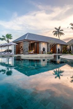 an outdoor swimming pool with lounge chairs and umbrellas next to the ocean at sunset