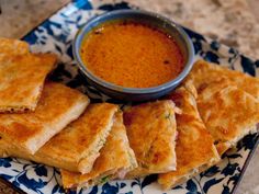 a blue and white plate topped with quesadillas next to a bowl of dipping sauce