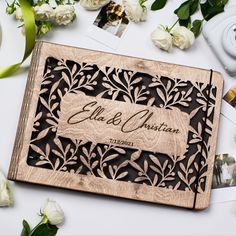 an engraved wooden wedding guest book surrounded by white flowers and greenery on a table