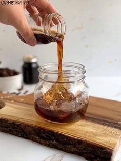 someone pouring syrup into a glass jar on top of a wooden cutting board with ice