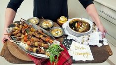 a man is holding a tray with food on it and the plate has skewered meats