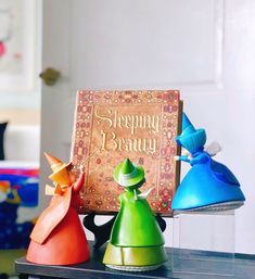 three colorful ceramic figurines sitting on top of a table next to a book