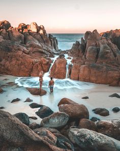 two people are standing in the water near some rocks