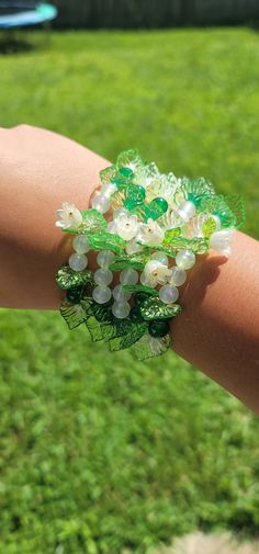 a woman's arm with green and white bracelets on top of it in the grass