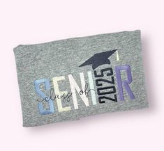 Seniors 2025 - Congrats!  Celebrate your Senior year with this embroidered shirt.  Embroidered letters in different colors with "Class of 2025" in dark charcoal.  Shirt is available in heather gray, white, light blue and light pink. Senior Shirt Ideas 2025 Trendy, Senior Shirt Designs, Seniors 2025, Senior Shirt Ideas, Senior Shirts, Embroidered Letters, Class Of 2025, Senior Year, Embroidered Shirt