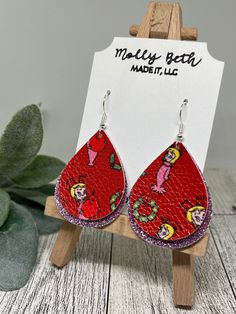 a pair of red leather earrings with cartoon characters on them, sitting on a wooden stand