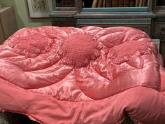 a pink comforter on a bed in front of a bookshelf and dresser