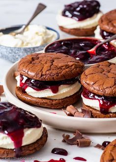 three cookies with ice cream and jelly on them are sitting on a plate next to other desserts