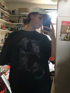 a young woman taking a selfie in her room with the door open and shelves full of clutter