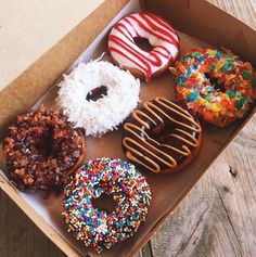 a box filled with lots of different flavored donuts on top of a wooden table