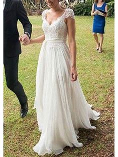 a man and woman holding hands walking in the grass with other people behind them wearing formal wear