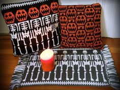 two crocheted pillows and a lit candle on a wooden floor next to each other