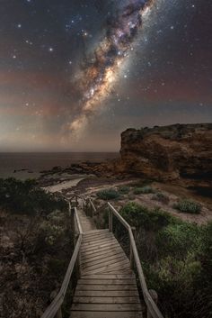 a wooden walkway leading to the beach under a night sky filled with stars and milky