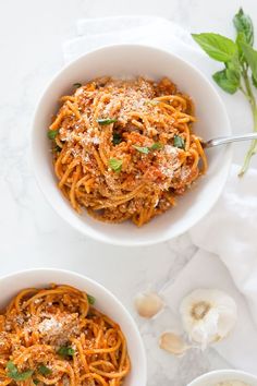 two white bowls filled with spaghetti and topped with parmesan cheese