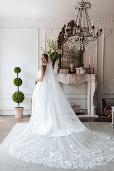 a woman in a wedding dress is standing near a table with potted plants and a chandelier