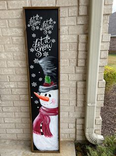 a snowman painted on the side of a brick wall next to a sign that says let it snow