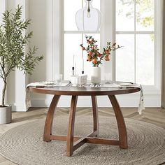 a round table with flowers and candles on it in front of a large window at the end of a room