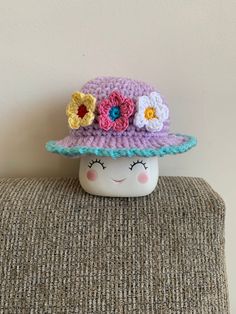 a crocheted hat with flowers on it sitting on top of a couch next to a wall