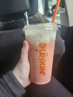 a person holding up a drink in the back seat of a car with an orange straw sticking out of it