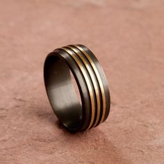 a black and gold wedding ring on a pink stone surface, with vertical stripes in the center