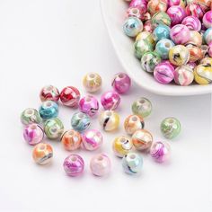 colorful glass beads in a bowl on a white table with one bead laying next to it