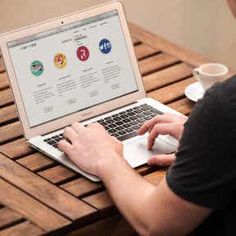 a man sitting at a wooden table using a laptop computer on top of a wooden table