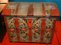 an old wooden chest with floral designs on the front and sides, sitting on a red floor