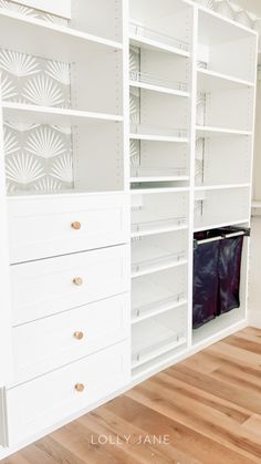 an empty closet with white shelves and drawers on the wall, next to a wooden floor