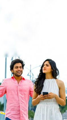 a man standing next to a woman holding a cell phone in her hand and looking up at the sky