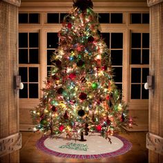 a brightly lit christmas tree in the corner of a room next to a large window