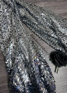 a black rose sitting on top of a table next to a silver sequin fabric