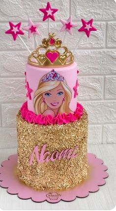 a pink and gold birthday cake with barbie on it's top, surrounded by stars