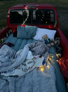 a bed in the back of a pick up truck with blankets and stuffed animals on it