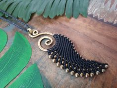 a black and gold beaded necklace sitting on top of a wooden table next to green leaves