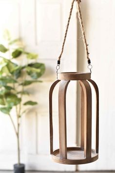 a wooden lantern hanging from a rope with a plant in the background and a white door behind it