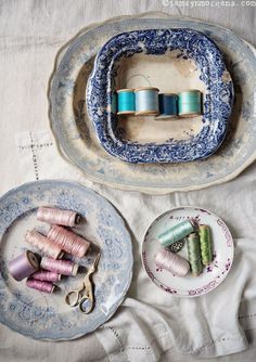 two plates with spools of thread sitting on top of each other next to a pair of scissors