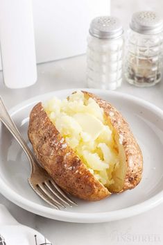 a baked potato on a plate with a fork and salt shaker next to it