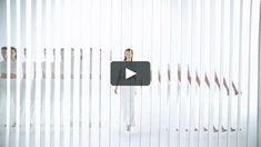 a woman standing in front of a white wall with vertical blinds on it's sides