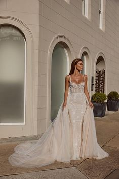 a woman in a wedding dress is standing on the sidewalk near a building and looking at the camera