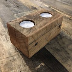 two candles are placed in a wooden box on the floor with wood planks behind them