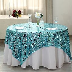 a table covered in blue sequins with wine glasses and flowers on the table