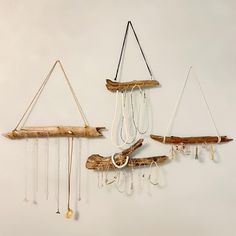 three pieces of driftwood are hanging on the wall with necklaces attached to them