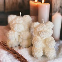 two white teddy bears sitting next to each other on a blanket with candles in the background