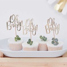 four cupcakes on a white plate with green leafy toppers and the words baby, oh boy